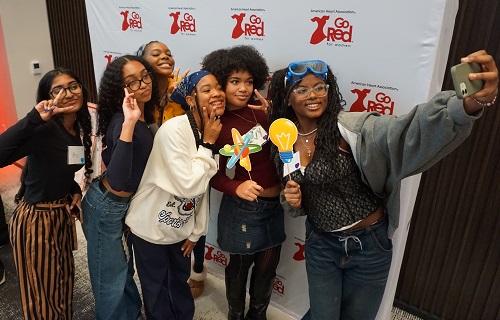 Six girls taking selfie in front of Go Red for Women banner